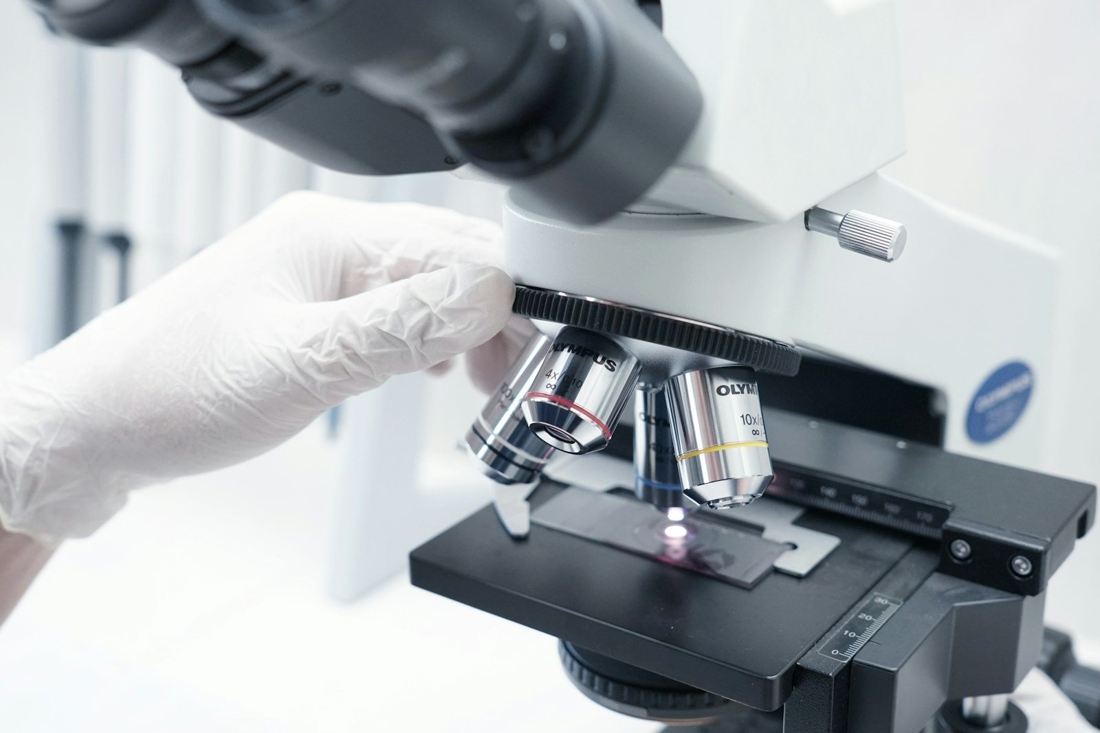 A gloved technician looking through a microscope