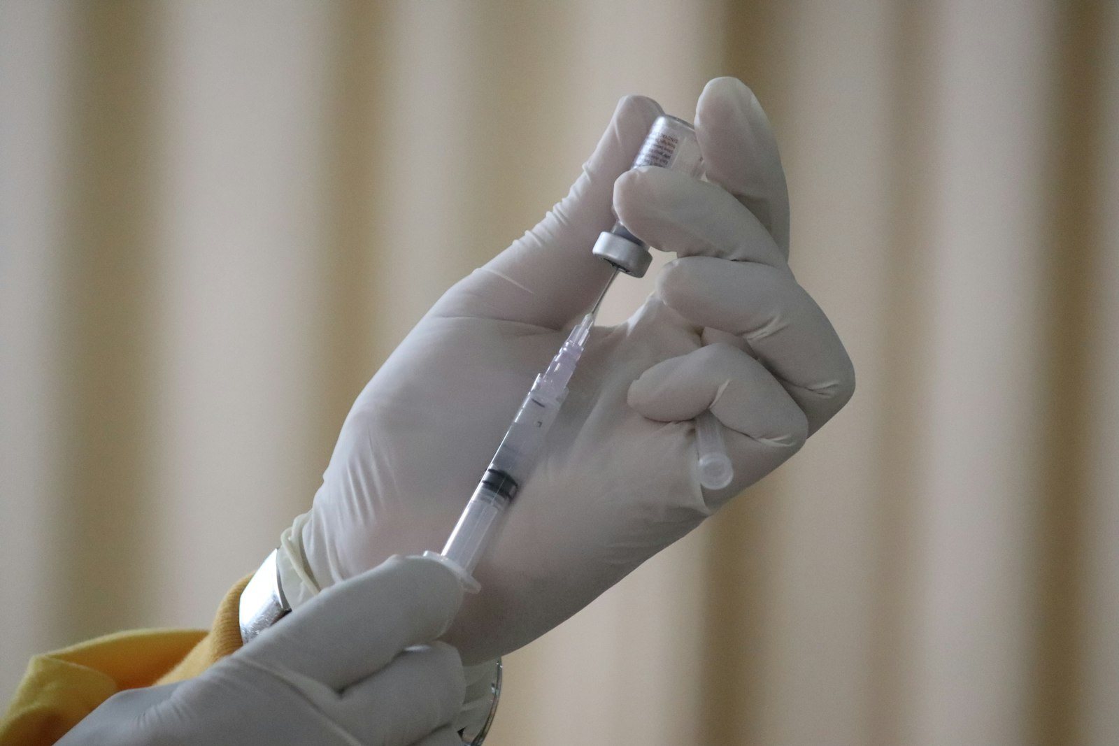 Gloved hands drawing liquid from a vial into a syringe