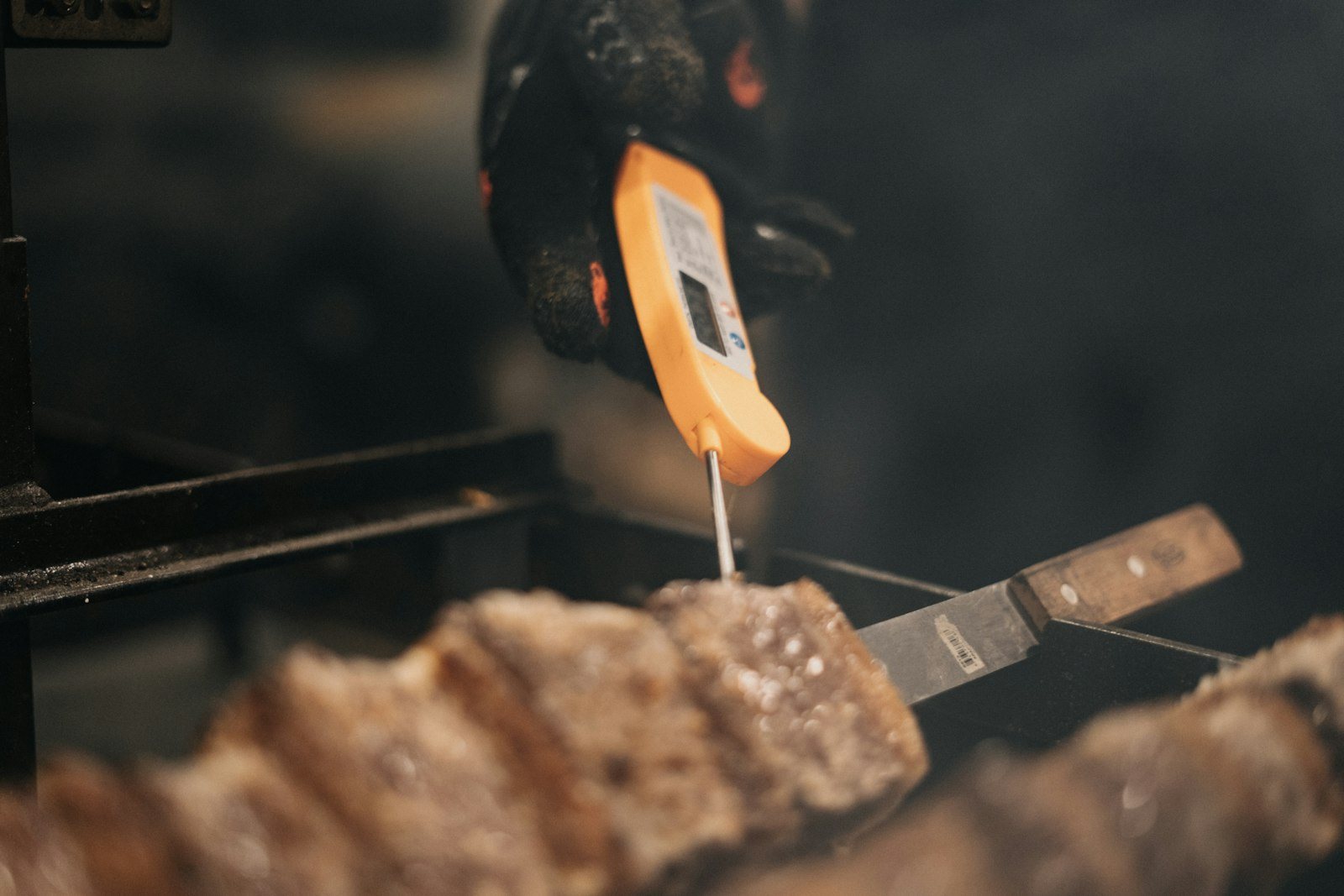 A probe thermometer inserted into meat on a grill