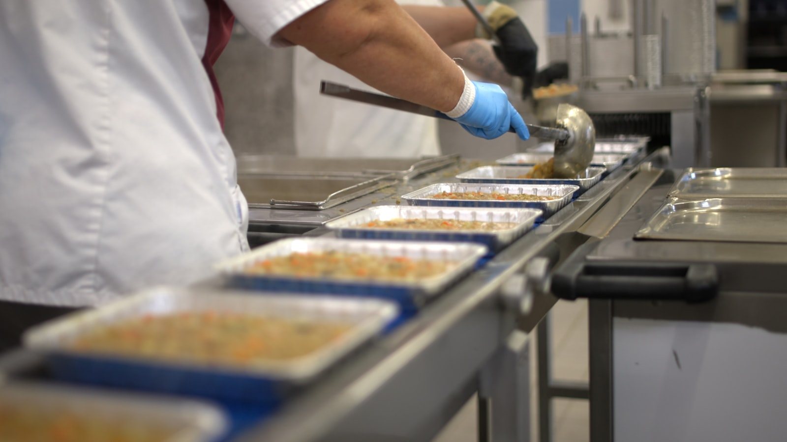A food worker filling trays in a commercial kitchen