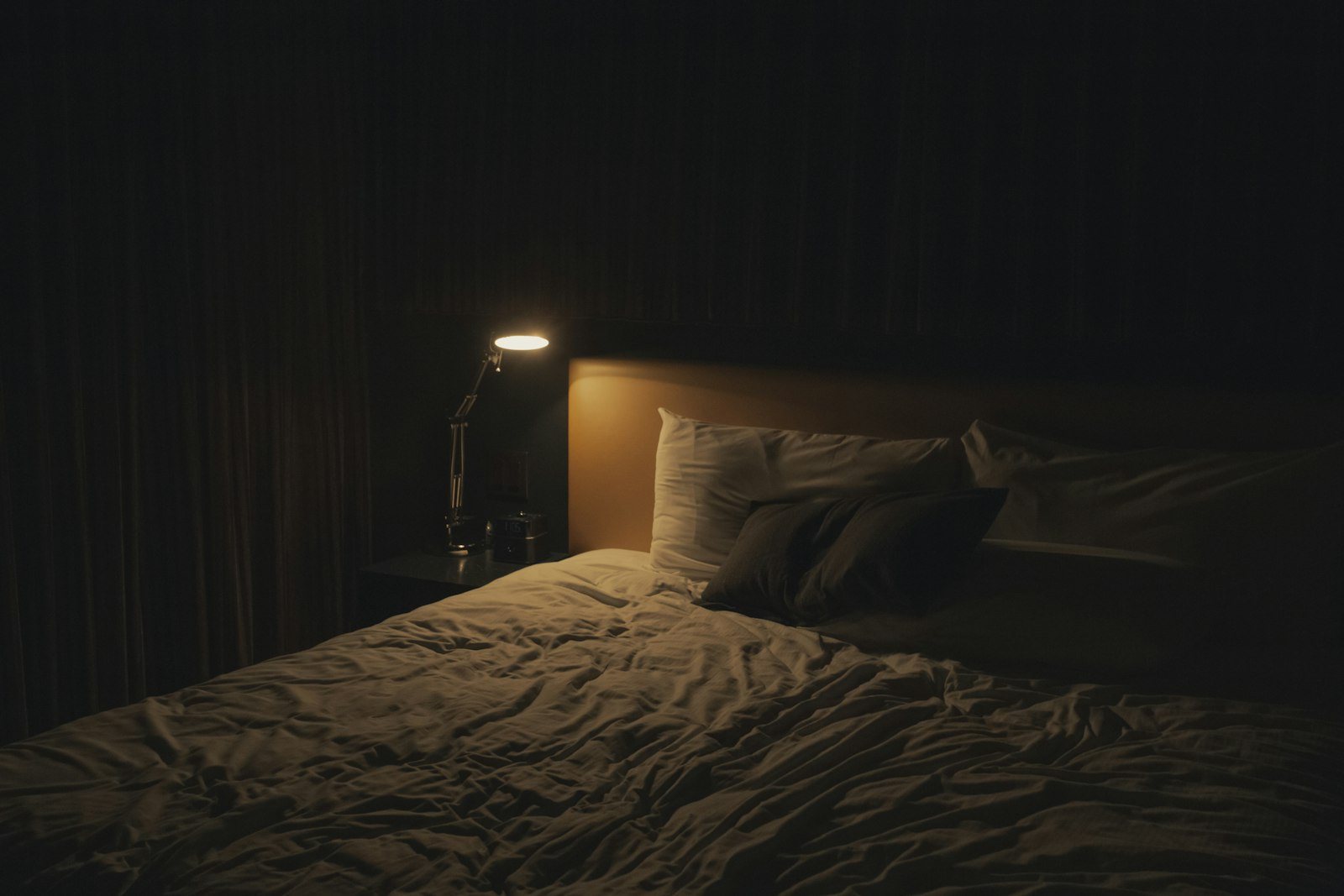 A bedside lamp lit in a dark bedroom